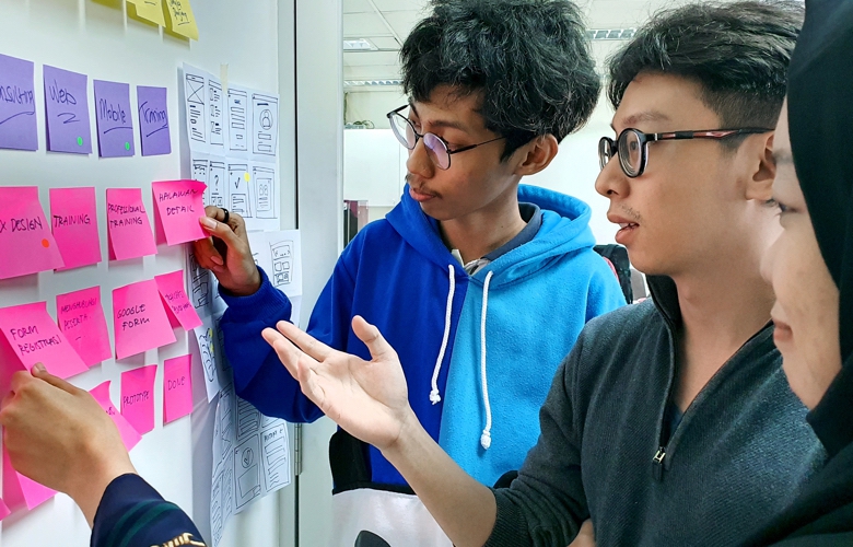 Three young business people placing colourful sticky notes on a whiteboard